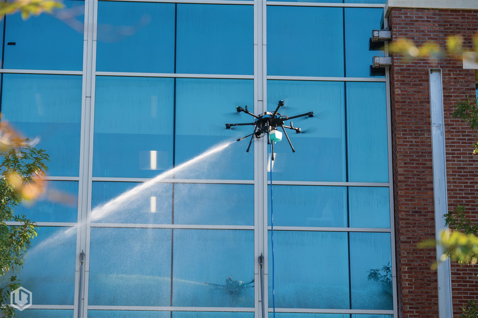 A Carolina Aerial Wash drone spraying a glass curtain-wall facade