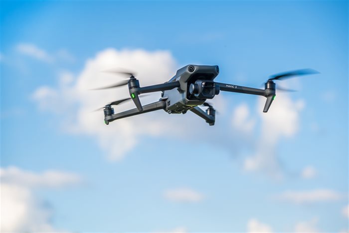 A survey drone in flight against a blue sky with clouds