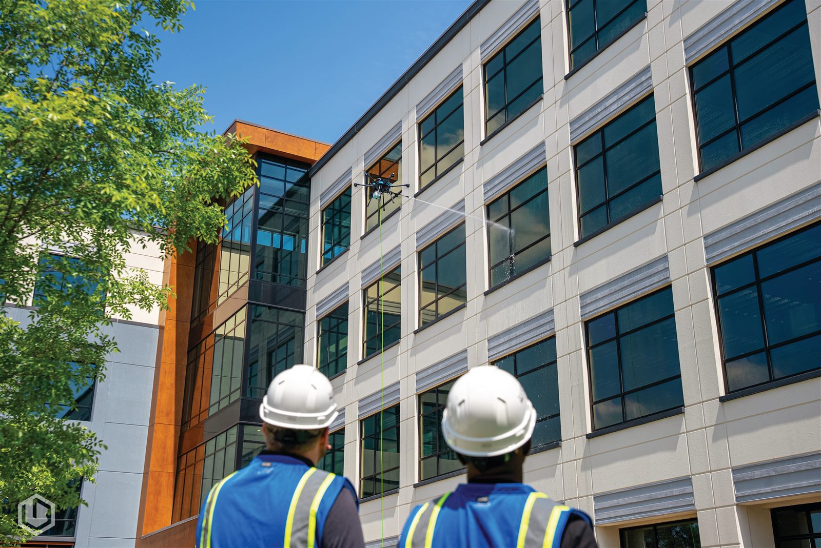 Two crew members watching the drone clean a multi-story building facade from a distance